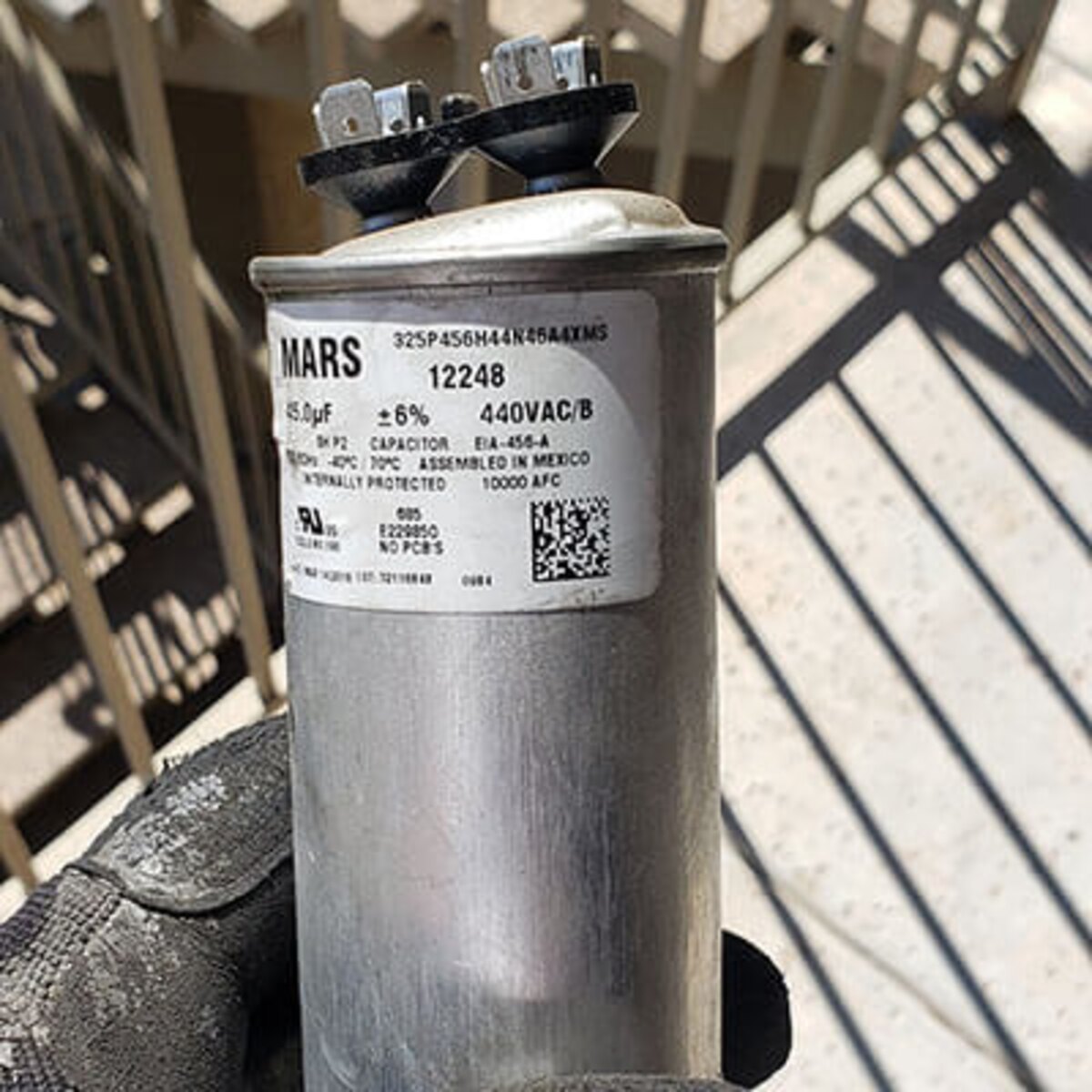 Close-up of a failed air conditioner capacitor with label and terminals