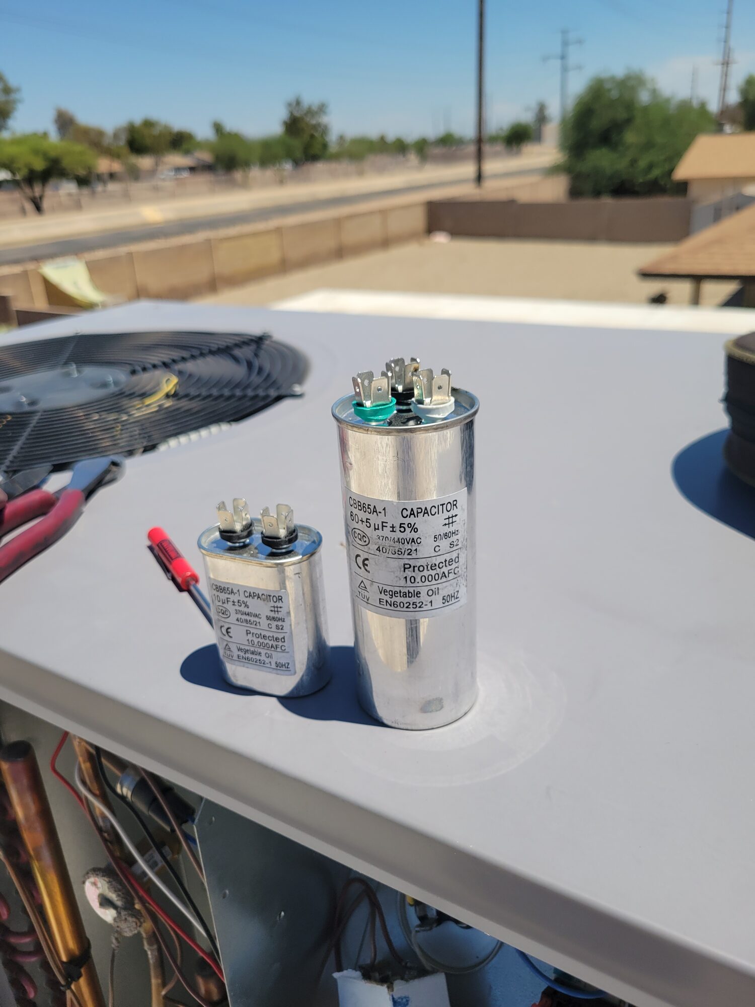 Two HVAC capacitors on top of an air conditioning unit